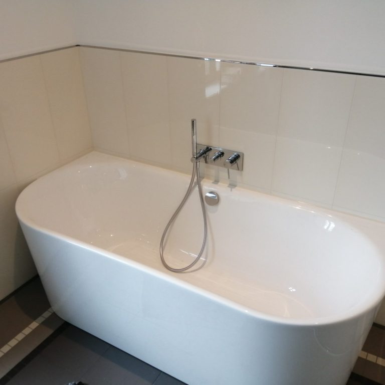 Moderne freistehende Badewanne mit verchromter Armatur in einem hellen Badezimmer.